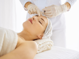 Obraz na płótnie Canvas Beautiful woman receiving beauty injections with closed eyes. Beautician doctor hands doing beauty procedure to female face with syringe