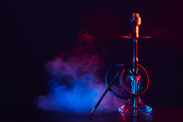 hookah with a glass flask and a metal bowl shisha with colored smoke on the table