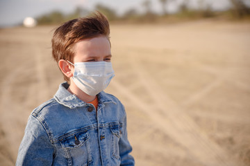 A boy of 8-9 years old in a protective mask outdoors  is upset and depressed due to the epidemic of...
