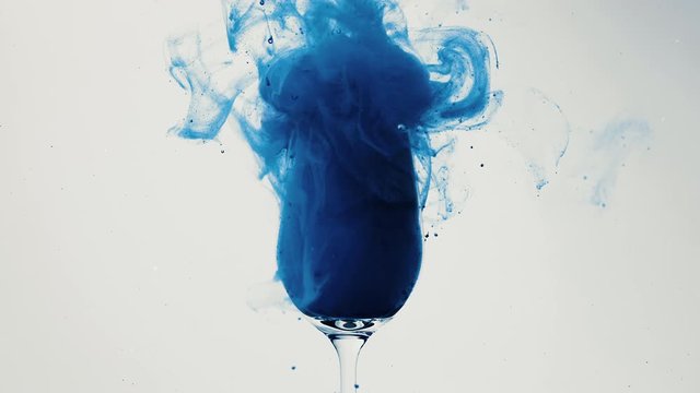 Blue liquid spilling into a wine glass on white background