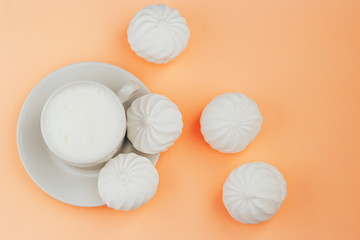 Cup of cappuccino and white marshmallows on orange background close up
