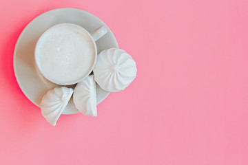 Top view on cup of milk and white marshmallows on pink background with copy space