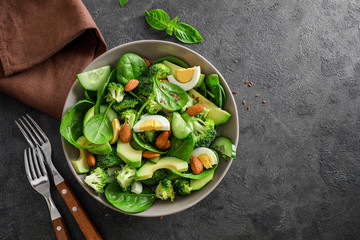 Avocado salad with boiled eggs, broccoli, spinach and almond nuts  in bowl on dark background. Top view.