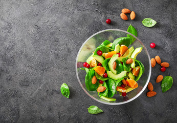 Avocado salad with spinach, oranges, red berries and almond nuts in glass bowl on dark background. Top view.