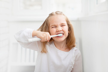 funny kid girl in the morning cleans the teeth electric toothbrush. The concept of daily care and hygiene of the oral cavity. prevention of dental caries.