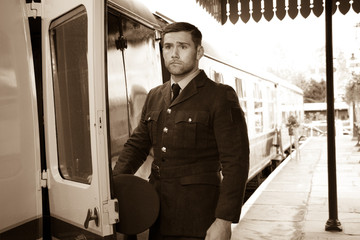 Handsome male British officer in vintage uniform at train station next to train