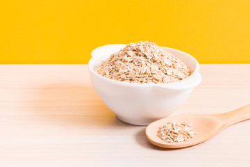 a white bowl with a oatmeal and a big wooden spoon on the table, yellow background, copy space