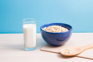 blue bowl with oatmeal, staak of milk and a large wooden spoon on a cutting board on a wooden table, blue background, proper nutrition and healthy lifestyle concept