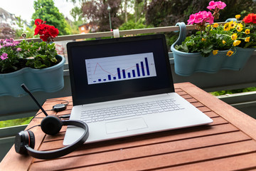 Home Office auf dem Balkon mit schönen Blumen am Notebook mit Headset auf Gartentisch zeigt die...