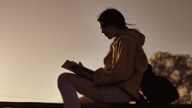 new kind of business remote online work freedom a concept with a backpack. silhouette lifestyle girl working in not at home. teenage girl with a digital tablet sits on a bench silhouette at sunset