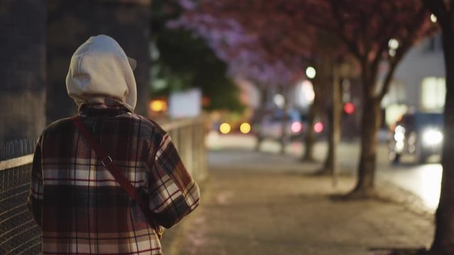 Back of young stylish woman in coat walking outside cold street city center at night. Female tourist. No other people. Loneliness in big town.