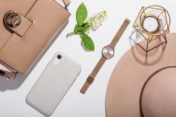 Fashion blog style desk with a collection of women's accessories: a gold watch, a phone, earrings, gloves, a hat and a handbag - on a white background. View from above, Flat lay.