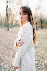 portrait of a young european fair haired girl in a light white dress and black shoes among a picturesque forest in autumn.nature,fashion concept.