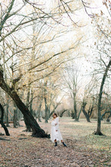 Fototapeta premium portrait of a young european fair haired girl in a light white dress and black shoes among a picturesque forest in autumn.nature,fashion concept.