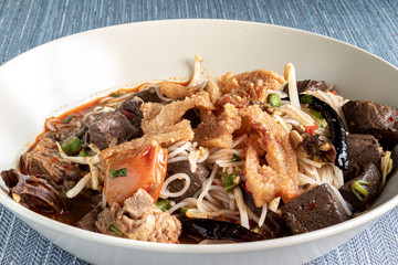 Burmese noodles with meat, liver, fried pork, tomato, mushroom, chili and other vegetables served on a plate