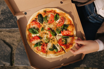 Top view image of couple grab slices of pizza from box at the outdoor. Man and woman hands taking pizza. Vegan pizza with fresh tomatoes basil and broccoli. Lactose and gluten free. Pizza box on