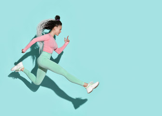 Fototapeta na wymiar Young beautiful smiling girl with modern hairstyle in sportswear and sneakers jumping running with legs stretched out
