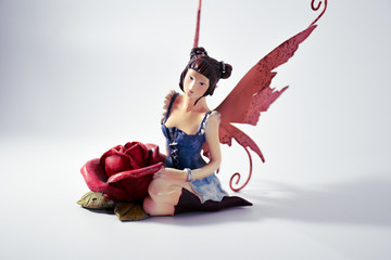 Small statue of a fairy sitting next to a rose
