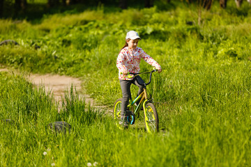 Portrait of a little girl on a bicycle in summer park outdoors