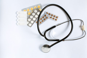 Medical supplies on a white background top view. stethoscope, multi-colored tablets and vitamins in plates