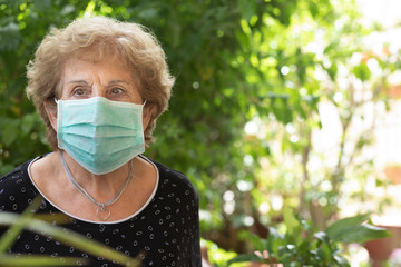 Anziana con mascherina chirurgica guarda seria nel suo giardino verde