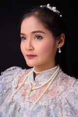 Young beautiful Asian woman wearing Thai traditional clothes against black background