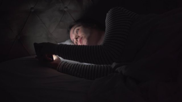 Young woman using mobile phone on the bed before she sleeping at night. Mobile addict or insomnia concept.
