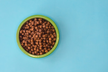 Pet dry food in a ceramic green bowl on pastel blue background. Dog, puppy or cat food. Top view, flat lay, copy space, place for text