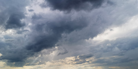 Obraz premium Dark stormy and windy sky before sundown,full of large gray-white fragmentary clouds with some sunbeams shining through holes in them.Tonal perspective.Horizontal banner,backdrop, texture or wallpaper