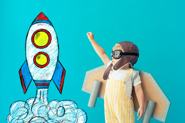 Happy child playing with toy paper wings against blue background © Igor Yaruta