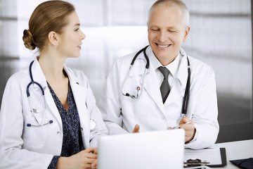 Elderly doctor and his female colleague discussing current disease therapy while sitting at working...