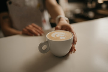 A female barista holds out a cup of hot latte to a client in a cafe. A waitress preparing a customer order.