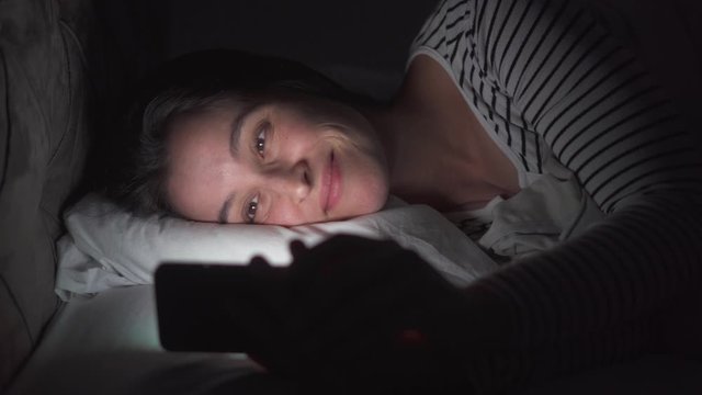 Young woman using mobile phone on the bed before she sleeping at night. Mobile addict or insomnia concept.

