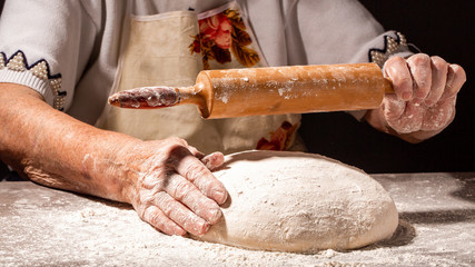 Beautiful and old women's hands knead the dough from which they will then make bread, pasta or pizza. A cloud of flour flies around like dust. Food concept.