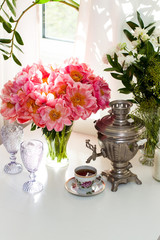 Still life with old russian samovar, rustic cup of tea, bouquet with peony flowers, glasses and candles.