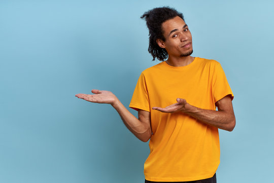 Positive cheerful African-American guy in yellow shirt shows screen with his both hand on the right on something useful. Concept of advertising goods in an online store. Places for advertising