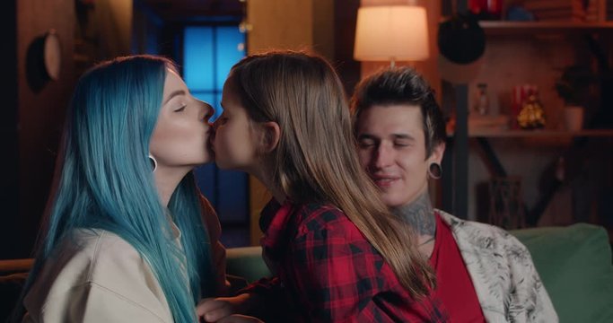 Millennial blue haired woman and her pretty daughter giving each other kiss while having fun and sitting on sofa with father.Portrait of happy modern family spending time together.