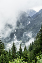 distant view of the Krimml Waterfalls between trees on a cloudy and foggy day in Austria. Highest waterfall in europe