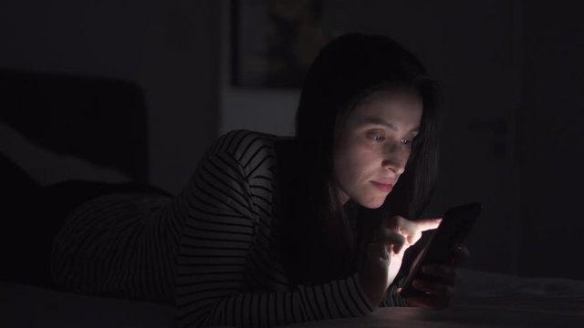 Woman is browsing social media in mobile phone at night on her bed
