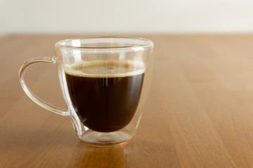 A glass with black coffee on the wooden table