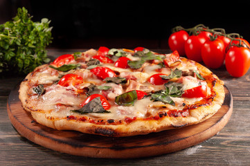 Homemade pizza with bacon and mushrooms on a wooden board. Tomatoes and basil.
