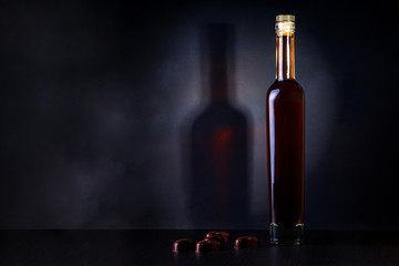 Fototapeta na wymiar bottle of brandy, whiskey and chocolate candies on a wooden table with a shadow from a bottle