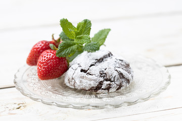 Homemade chocolate crinkles and strawberry in a glass saucer.
