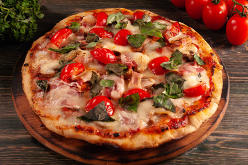 Homemade pizza with bacon and mushrooms on a wooden board. Tomatoes and basil.
