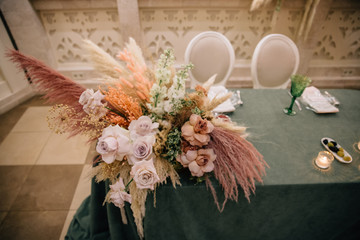wedding table setting for the bride and groom in an emerald tablecloth, cream shades of napkins, fresh flowers and pampas grass in cream shades