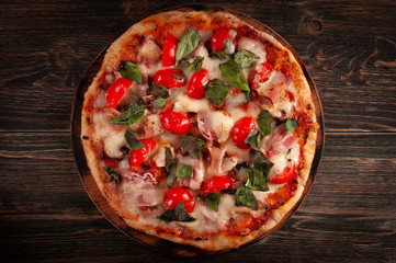 Homemade pizza with bacon and mushrooms on a wooden board. Tomatoes and basil.