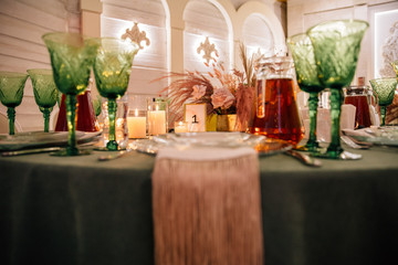 wedding table setting for guests made of emerald-colored tablecloths, cream shades of napkins, fresh flowers and pampas grass in cream shades