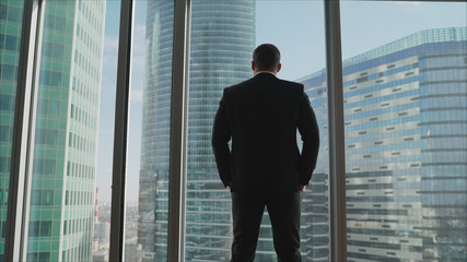  looking into the distance to the city. Successful man stands in the neoboksreb. A businessman stands in front of a window and looks into it.