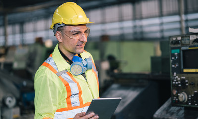 Fototapeta premium worker man caucasian in protective safety jumpsuit uniform and with hardhat and using digital tablet at factory.Metalworking industry concept professional engineer in tool manufacturing workshop