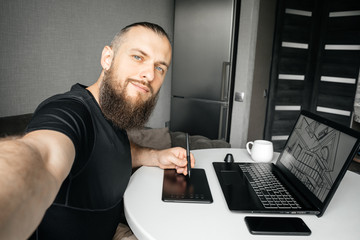 Selfie bearded young designer at his workplace at home. Remote work. Freelance